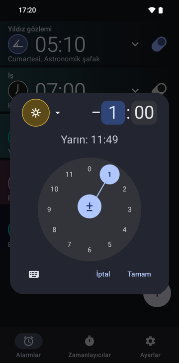Alarm listesinin üzerinde açık Risetime alarm oluşturma penceresi: altın rengi Noon çıpa simgesi, saat alanı seçili eksi 1 saat 00 dakikalık bir fark ve Tomorrow: 11:49 satırı. Alt yarıyı 1'in seçili olduğu dairesel bir saat kadranı doldurur; altında bir klavye düğmesi, Cancel ve OK var.